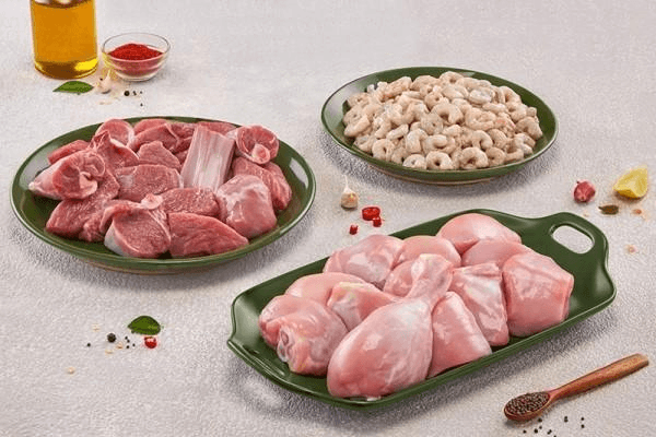 Raw mutton, chicken, and prawns on green plates with spices on a grey counter