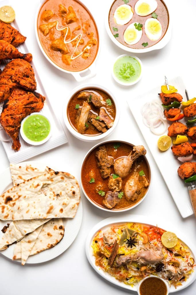 Indian feast spread: tandoori, curries, biryani, naan, and sides on a white table