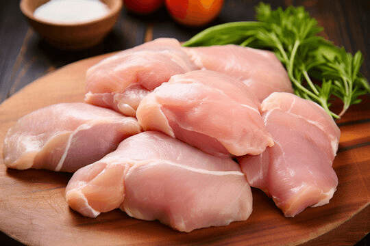 Raw boneless chicken pieces on a wooden board with fresh herbs